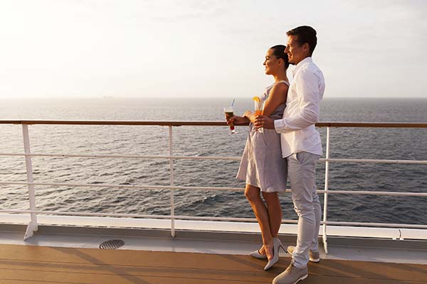 side view of smiling couple having cocktails on cruise ship at sunset