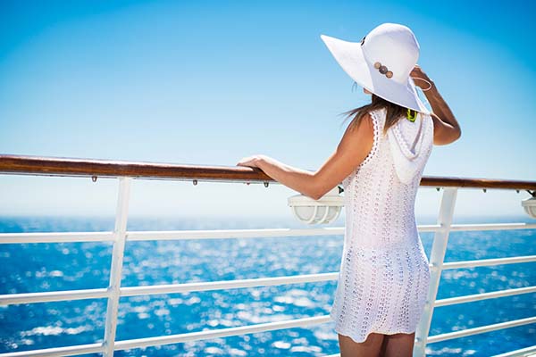 Unrecognizable woman with hat on a cruise ship looking at the view.