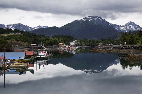Halibut Cove Alaska taken on overcast day with mountains and other structures reflected on water.