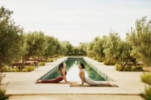 Wide shot friends performing sunrise yoga beside luxury resort pool -cm