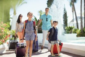 Family with suitcases passing by fountain in tourist resort-cm