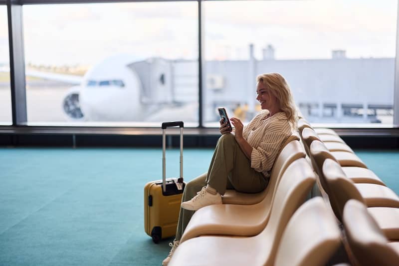 Happy female tourist using cell phone at airport terminal.-cm
