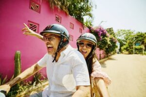 Medium shot mischievous senior couple driving motor scooter on street-cm