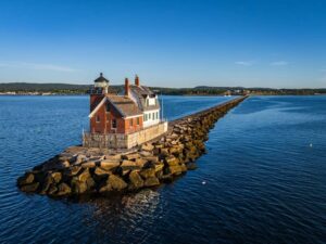 Scenic view of a historic lighthouse on a rocky breakwater extending into the calm blue sea under a clear sky -cm