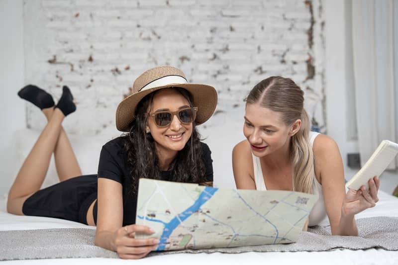 Two young adult women planning travel itinerary with map-cm