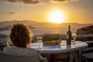 Woman with glass of wine enjoying sunset over Naxos town, with Paros Island in the background, Greece -cm